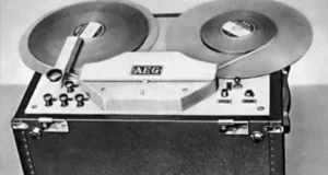 Black and white photograph of an early AEG Magnetophon, one of the first reel-to-reel tape recorders developed in the 1930s. The device features two large reels, control knobs, and a sturdy, box-like casing. This pioneering technology played a crucial role in the advancement of audio recording, setting the foundation for modern magnetic tape recording methods.