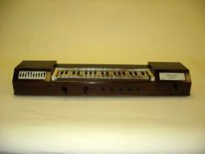 A vintage Ondioline, an early electronic keyboard instrument invented by Georges Jenny in 1940. The wooden instrument features a compact keyboard with black and white keys, multiple control knobs, and labeled switches on the left side for sound modulation.