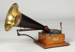 A vintage American Berliner Gramophone from 1931, featuring a wooden base, a black metal horn with a brass interior, and a manual crank. This early record player was a significant innovation in sound recording and playback technology.